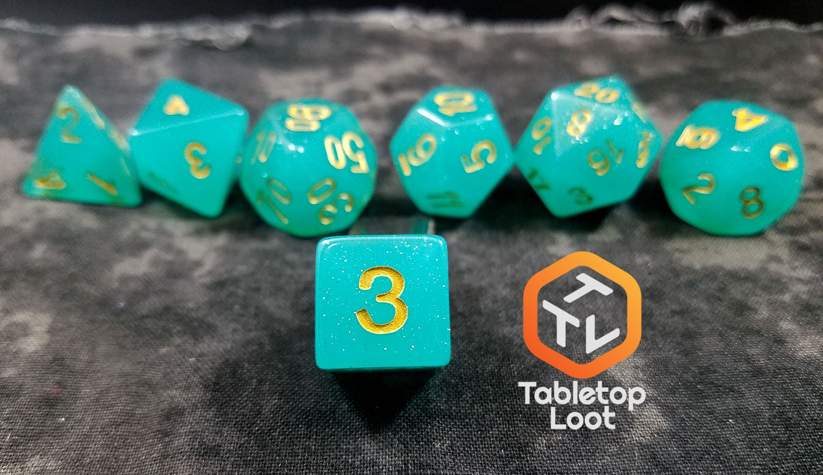A close up of the D6 from the Blue Beryl 7 piece dice set from Tabletop Loot with a bright glittery aqua resin and gold numbering.