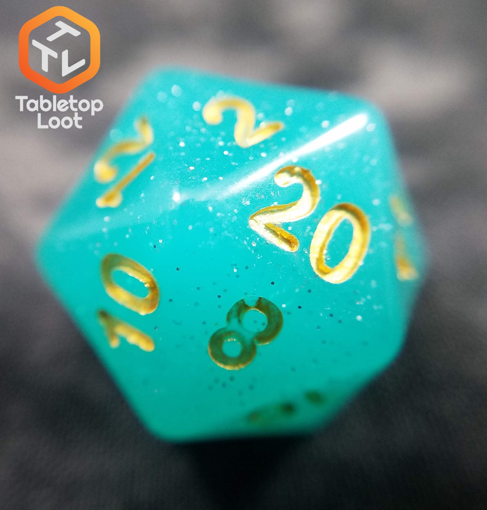 A close up of the D20 from the Blue Beryl 7 piece dice set from Tabletop Loot with a bright glittery aqua resin and gold numbering.