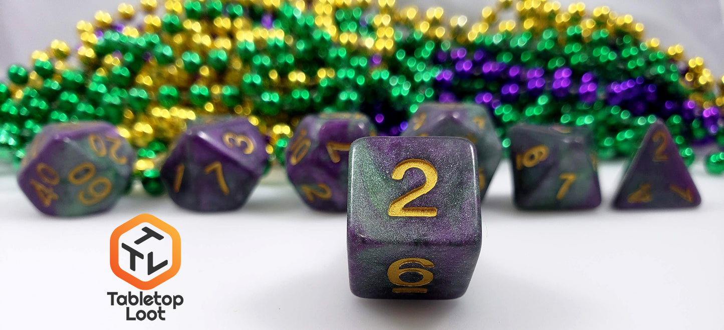 A close up of the D6 from the King Cake 7 piece dice set from Tabletop Loot with swirls of green and purple shimmery resin and gold numbering.