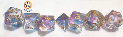 The Misty Step 7 piece dice set from Tabletop Loot with swirls of purple and blue in clear resin with gold numbers.