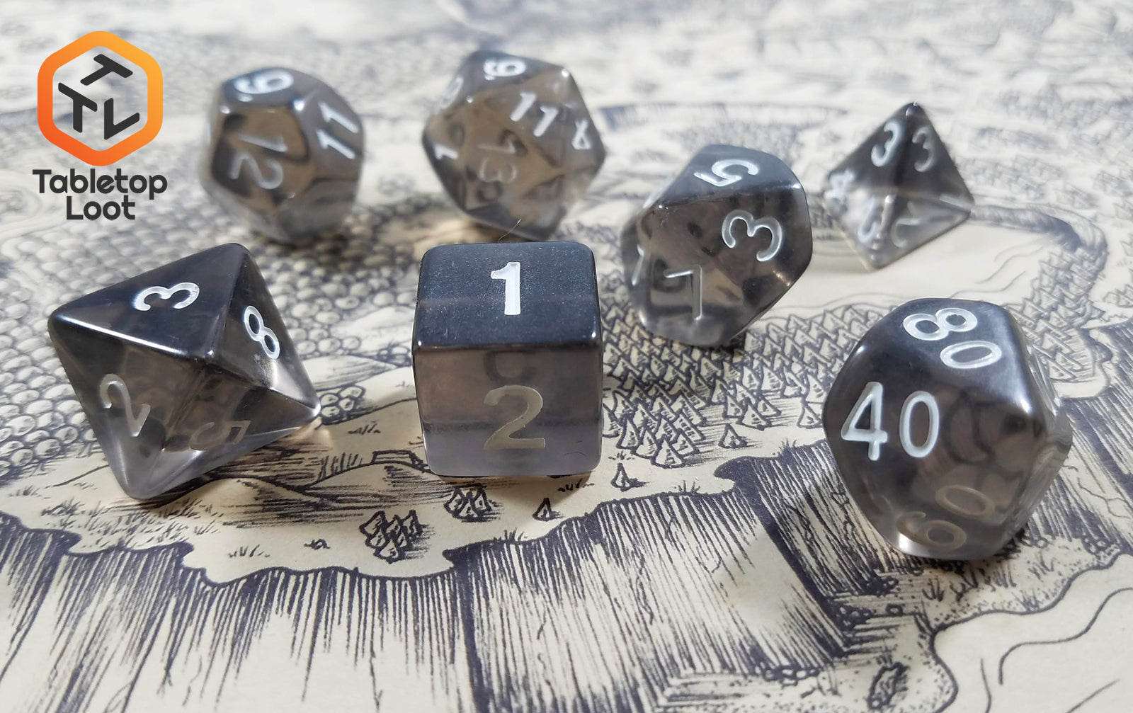 The Shadow Thrall 7 piece dice set from Tabletop Loot; grey tinted like smoky quartz with white numbering.