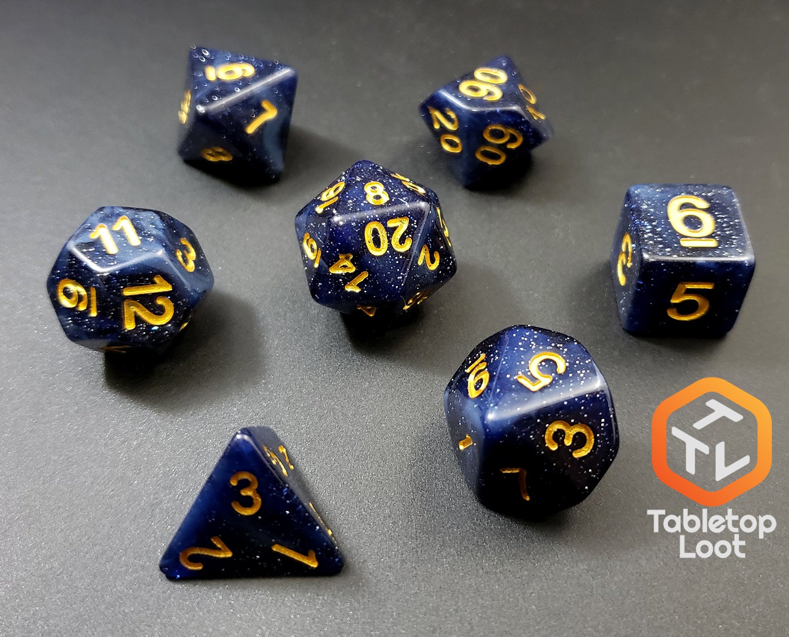 The Starry Twilight 7 piece dice set from Tabletop Loot, with an opaque deep navy resin filled with gold glitter and inked in gold.
