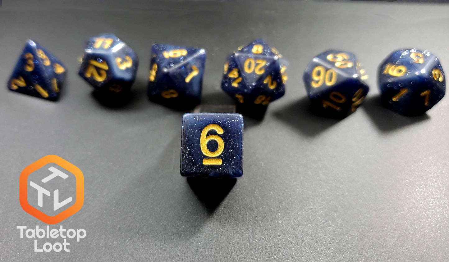 A close up of the D6 from the Starry Twilight 7 piece dice set from Tabletop Loot, with an opaque deep navy resin filled with gold glitter and inked in gold.