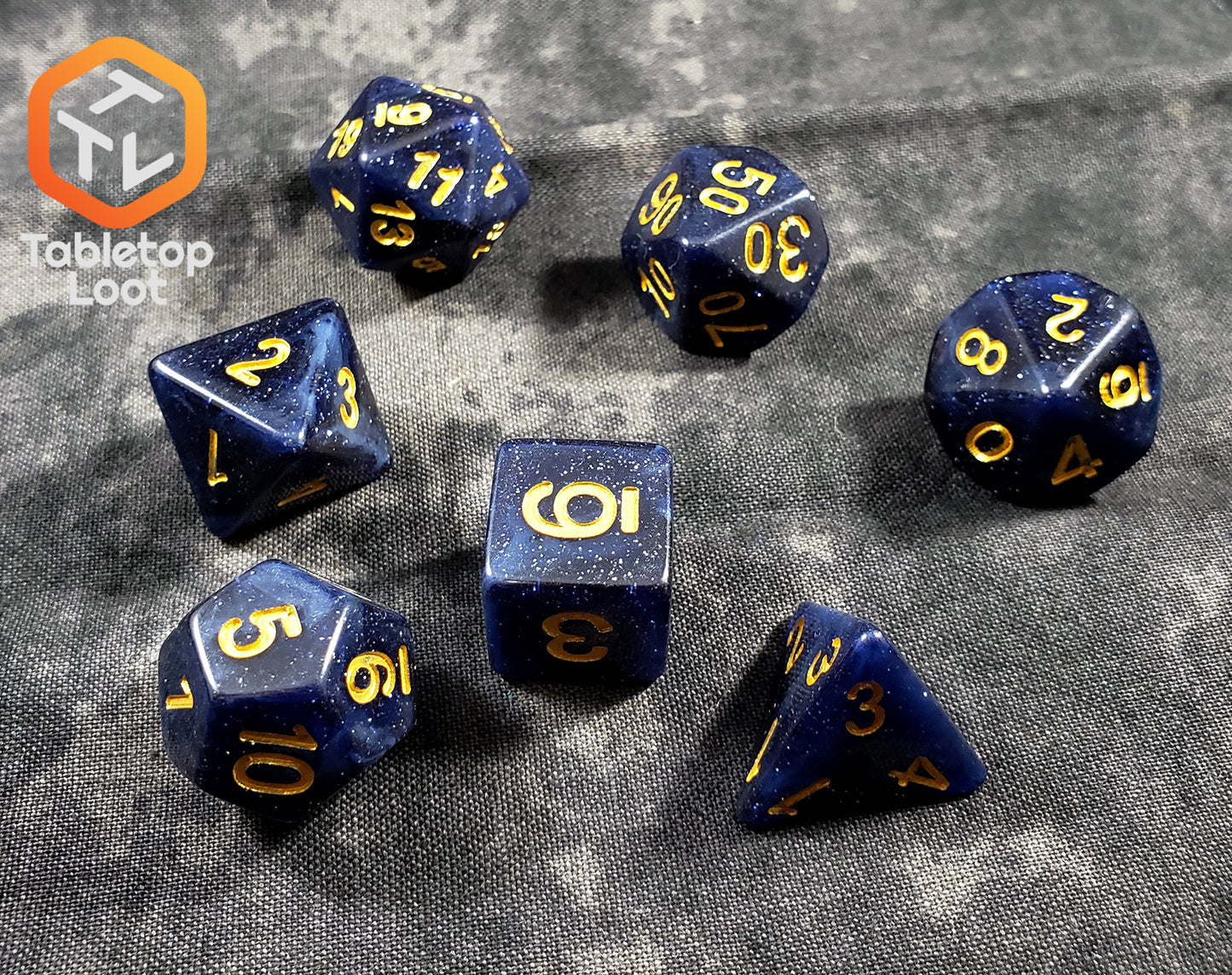 The Starry Twilight 7 piece dice set from Tabletop Loot, with an opaque deep navy resin filled with gold glitter and inked in gold.
