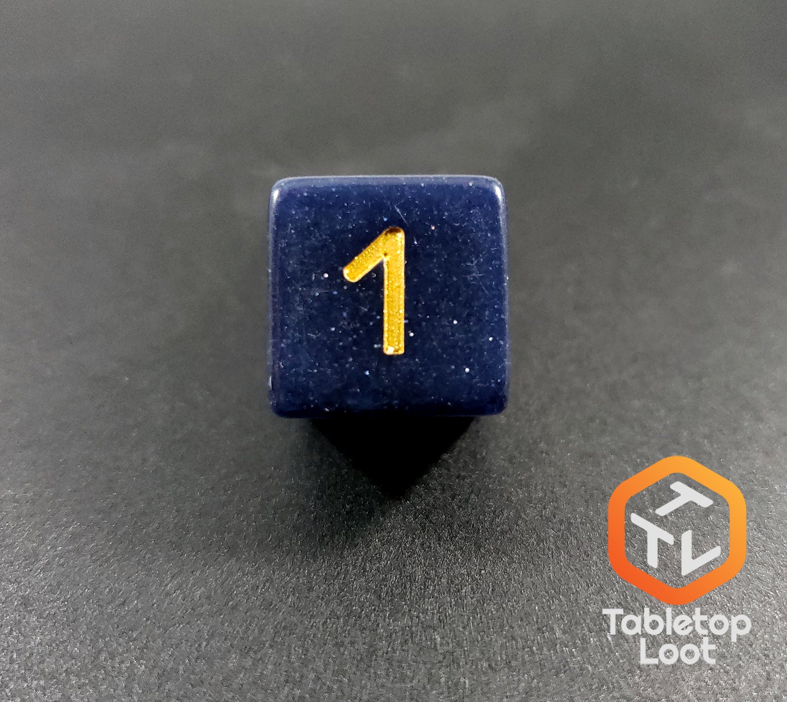 A close up of the D6 from the Starry Twilight 7 piece dice set from Tabletop Loot, with an opaque deep navy resin filled with gold glitter and inked in gold.