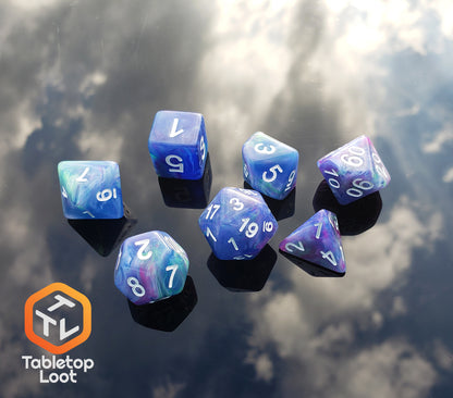 The Dancing Lights 7 piece dice set from Tabletop Loot with swirls of purple, pink, green, teal, and blue resin and white numbers.