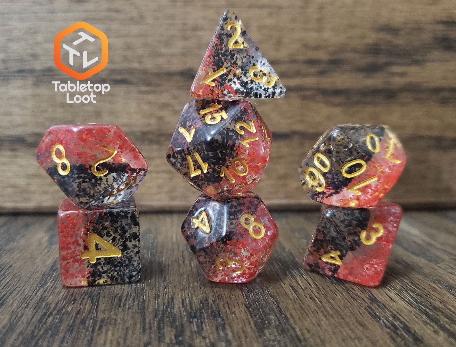 The Contagion 7 piece dice set from Tabletop Loot with black and red speckles suspended in clear and gold numbering.