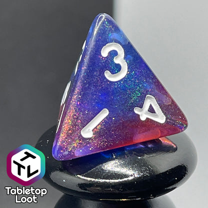 A close up of the D4 from the Transmutation 7 piece dice set from Tabletop Loot with swirls of blue and red appearing purple in some spots, filled with iridescent glitter adding little rainbows in places, and inked in white.