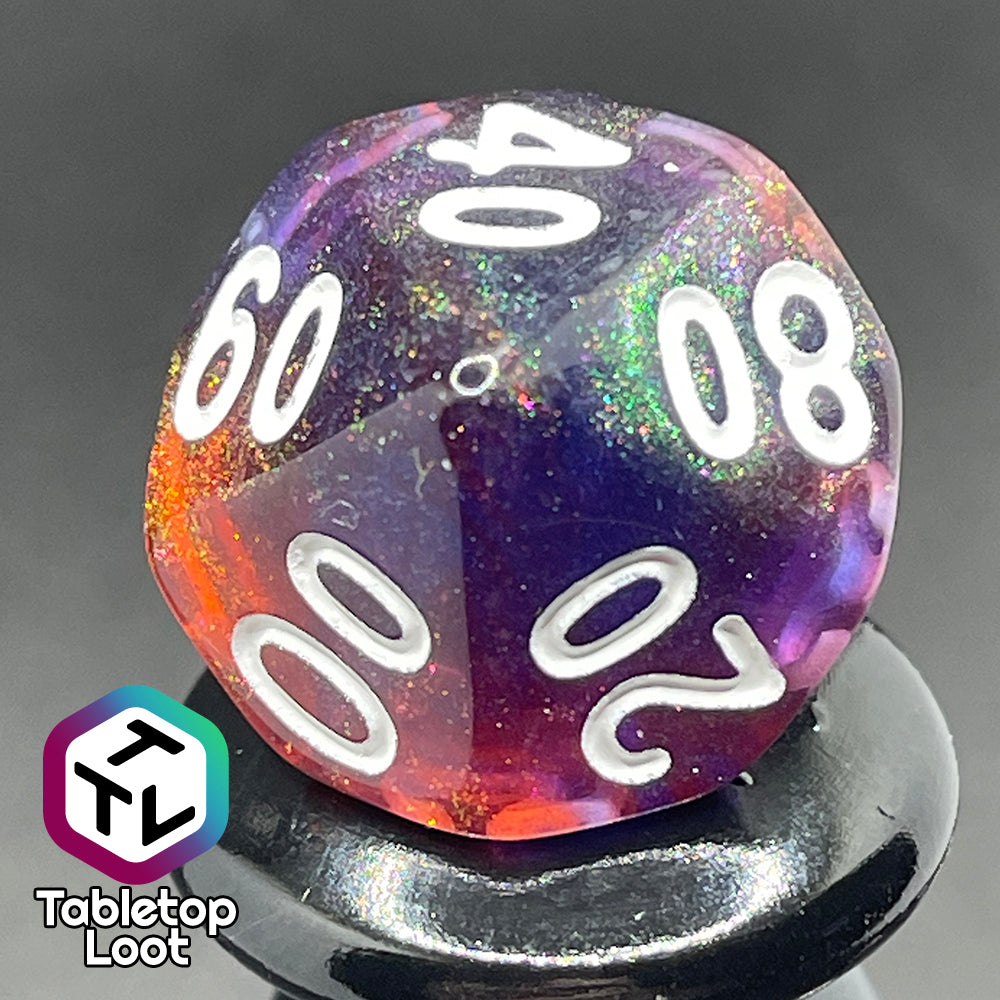 A close up of the percentile die from the Transmutation 7 piece dice set from Tabletop Loot with swirls of blue and red appearing purple in some spots, filled with iridescent glitter adding little rainbows in places, and inked in white.