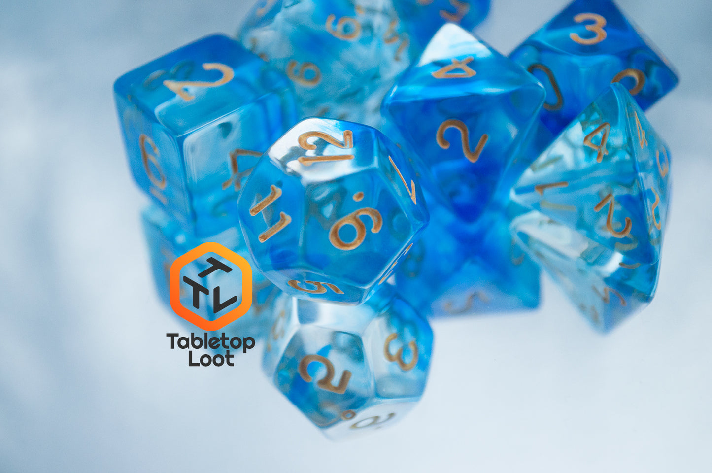 A close up of the Under the Sea 7 piece dice set from Tabletop Loot with swirls of blue and gold numbering.