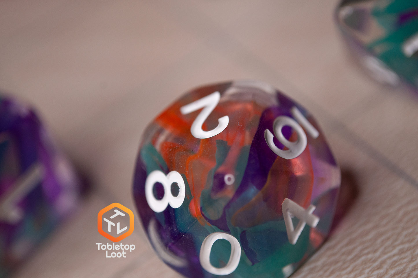 A close up of the Raise the Banners D10 with orange, blue, and purple ribbons of color swirled inside clear resin.
