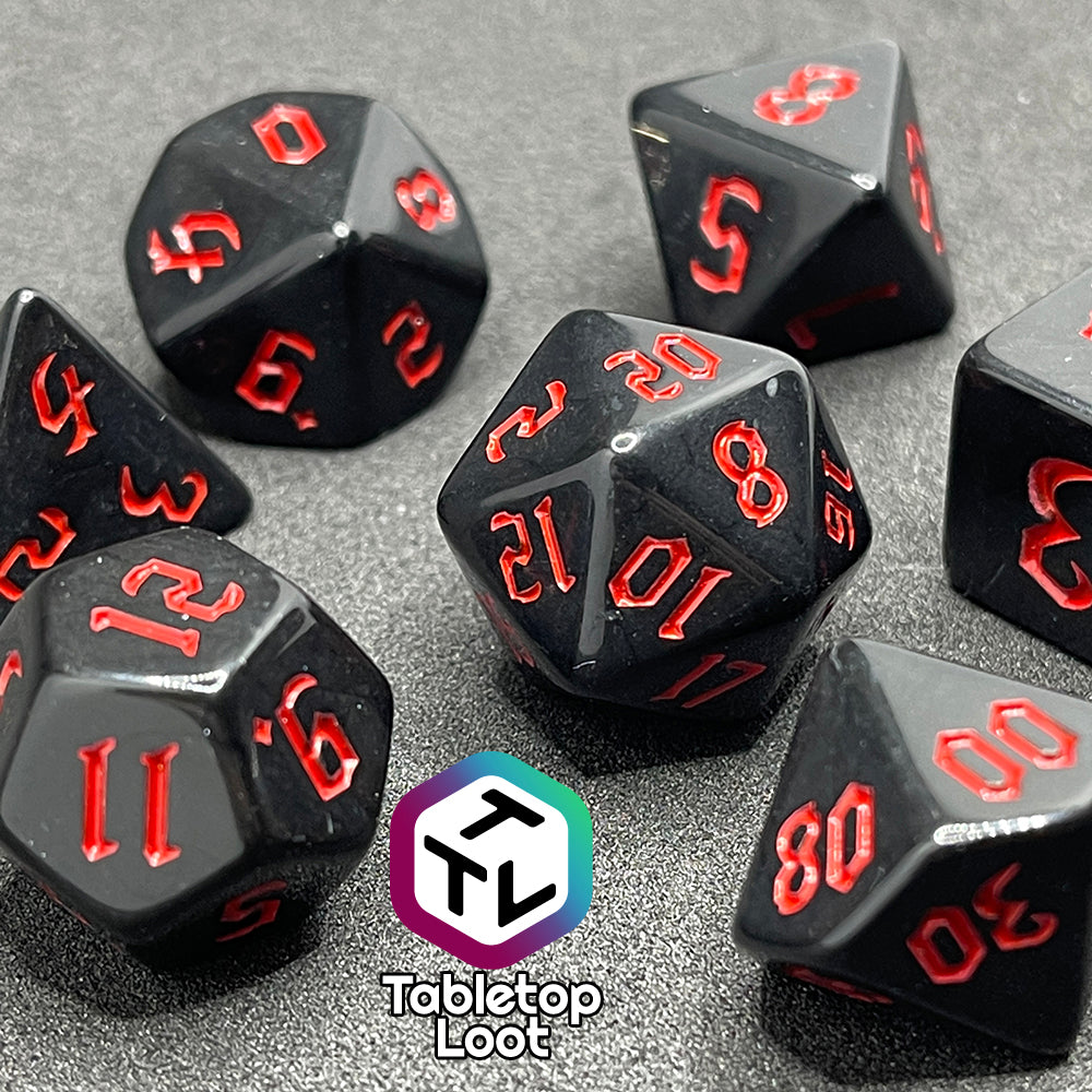 A close up of the Vampiric Touch 7 piece dice set from Tabletop Loot; reflective black with red numbering in a bold gothic font.