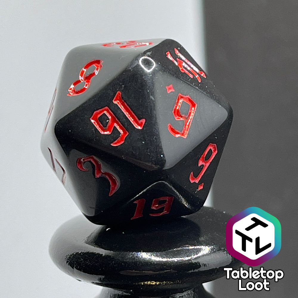 A close up of the D20 from the Vampiric Touch 7 piece dice set from Tabletop Loot; reflective black with red numbering in a bold gothic font.