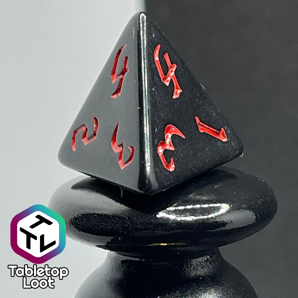A close up of the D4 from the Vampiric Touch 7 piece dice set from Tabletop Loot; reflective black with red numbering in a bold gothic font.