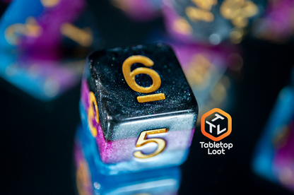 A close up of the Pulse Wave D6 made with blue, purple, and black stripes of color and lots of glitter, inked in gold.