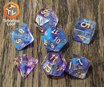 The Infestation 7 piece dice set from Tabletop Loot with swirls of blue and purple and dark speckles suspended in a clear resin with gold numbering.