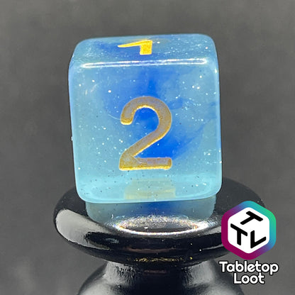 A close up of the D6 from the Water Genasi 7 piece dice set from Tabletop Loot with lots of glitter in two toned blue swirls and gold numbering.