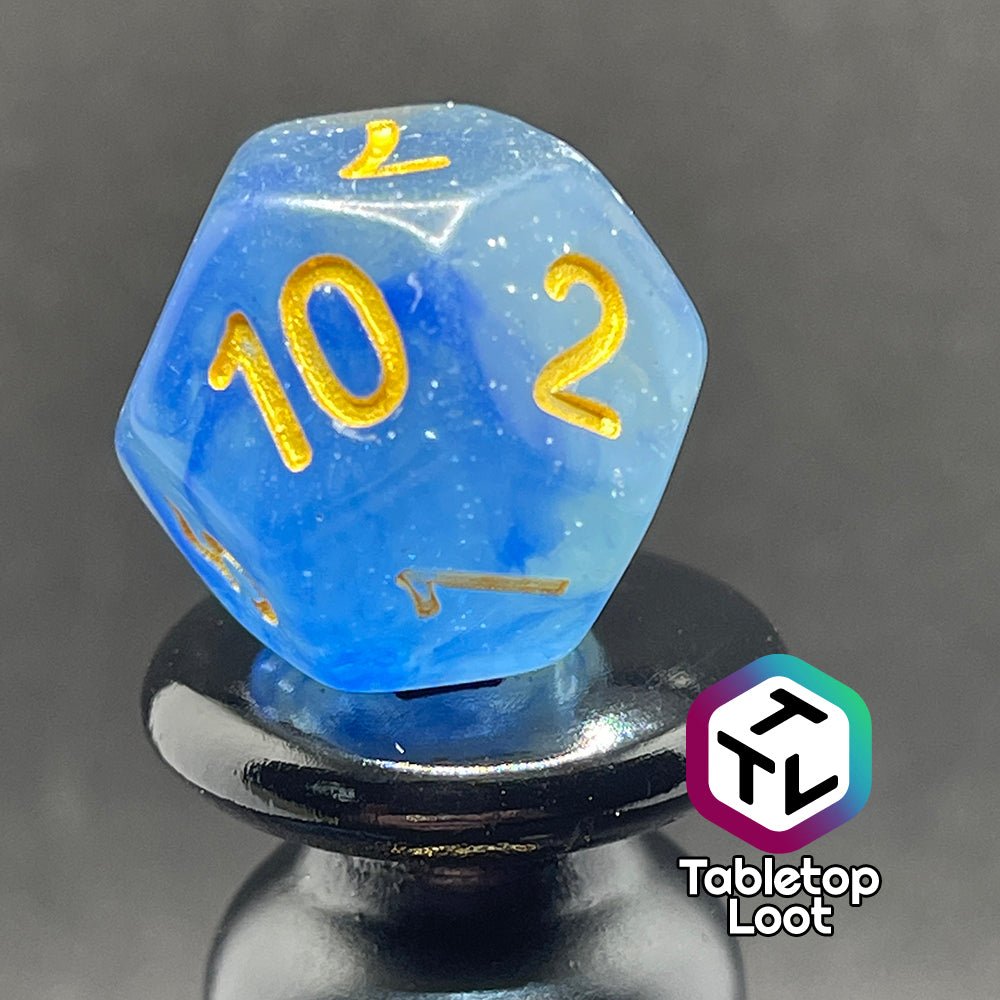 A close up of the D12 from the Water Genasi 7 piece dice set from Tabletop Loot with lots of glitter in two toned blue swirls and gold numbering.