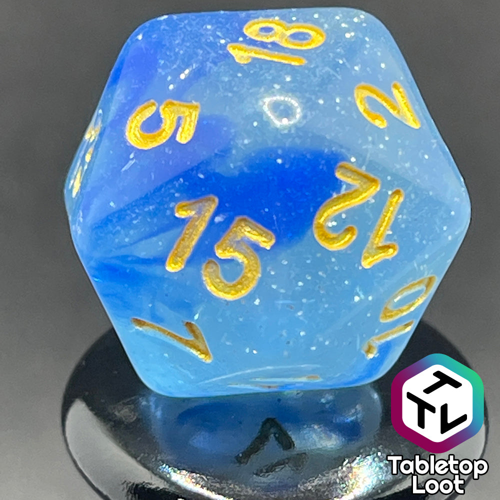 A close up of the D20 from the Water Genasi 7 piece dice set from Tabletop Loot with lots of glitter in two toned blue swirls and gold numbering.
