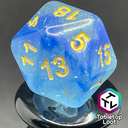 A close up of the D20 from the Water Genasi 7 piece dice set from Tabletop Loot with lots of glitter in two toned blue swirls and gold numbering.