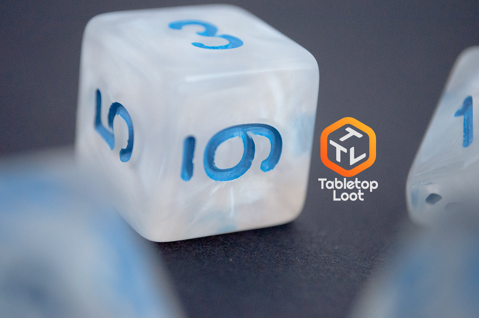 A close up of the D6 from the Dinneshere 7 piece dice set from Tabletop Loot with wispy white swirls and blue numbering.