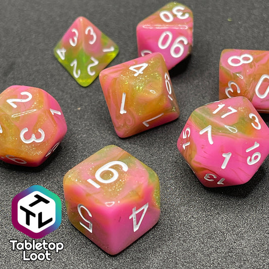 A close up of the Wither and Bloom 7 piece dice set with bright pink and glittery green swirls and white numbering.