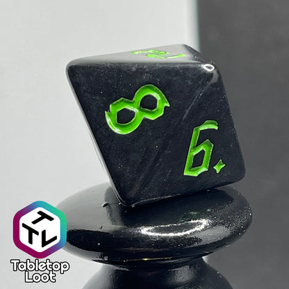 A close up of the D8 from the Xenomorph 7 piece dice set from Tabletop Loot with bright green bold gothic numbers on highly reflective black dice.