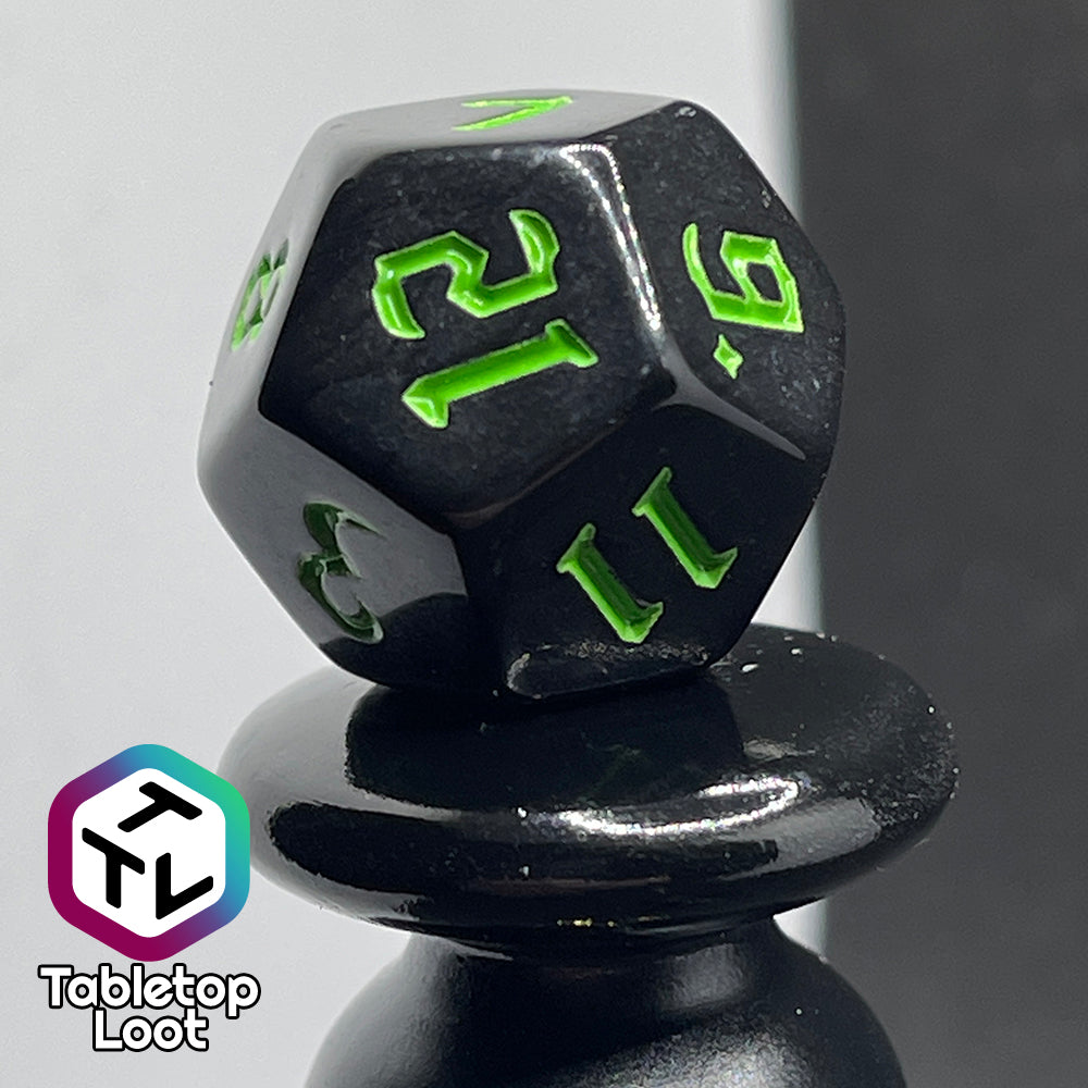 A close up of the D12 from the Xenomorph 7 piece dice set from Tabletop Loot with bright green bold gothic numbers on highly reflective black dice.