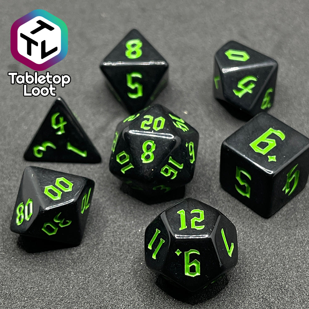 A close up of the Xenomorph 7 piece dice set from Tabletop Loot with bright green bold gothic numbers on highly reflective black dice.
