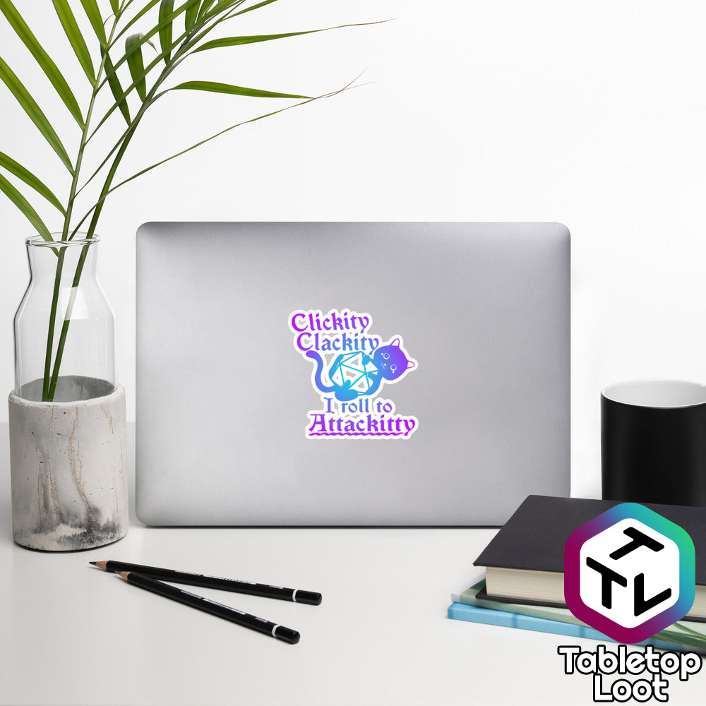 A 4 inch sticker from Tabletop Loot says "Clickity clackity, I roll to Attackitty" in a purple and blue Old English font with a cat holding onto a D20 between lines of text.