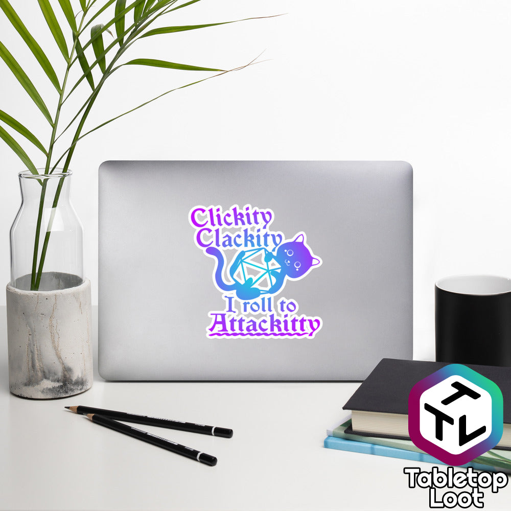 A 5.5 inch sticker from Tabletop Loot says "Clickity clackity, I roll to Attackitty" in a purple and blue Old English font with a cat holding onto a D20 between lines of text.