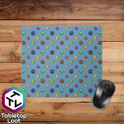 A smaller 18 by 16 inch desk and mouse pad has a polyhedral dice pattern in red, brown, yellow, teal, blue, and purple on a blue background.