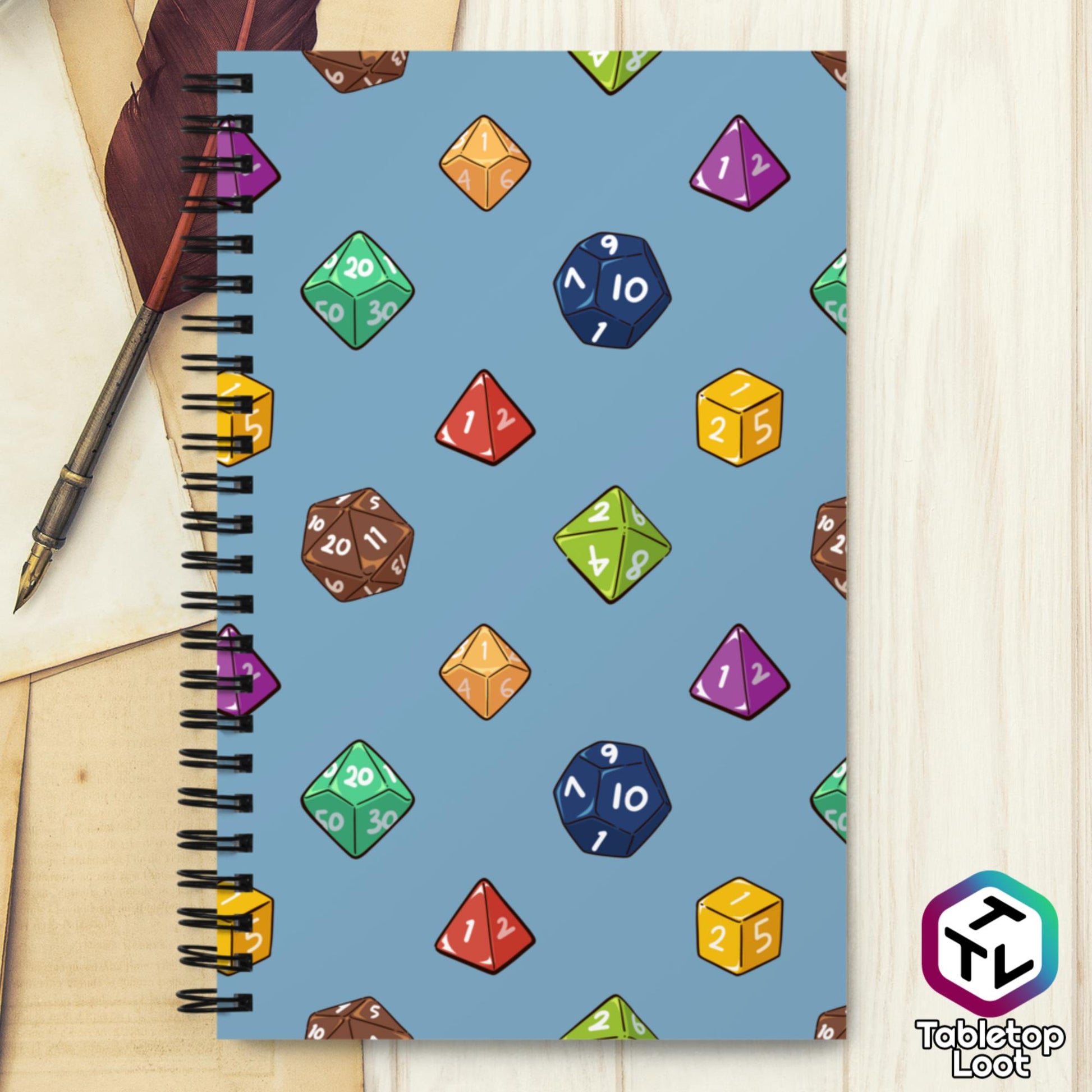 A spiral notebook has a polyhedral dice pattern in red, brown, yellow, teal, blue, and purple on a blue background.